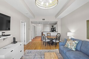 A modern living room with a flat-screen TV, a blue sofa with patterned cushions, and a wooden coffee table. - 🌅 Madeira Bay 407 | Beach Getaway Just Steps from the Sand (Madeira Beach)
