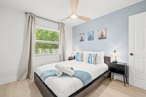 A bedroom with a bed, a nightstand, a ceiling fan, a window with curtains, and wall art. - Coastal Getaway - 13 Min to Beach - Bike Trail (Belleair)