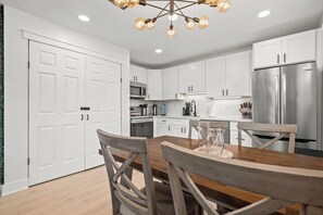 A modern kitchen with white cabinets, stainless steel appliances, and a wooden dining table. - Coastal Getaway - 13 Min to Beach - Bike Trail (Belleair)