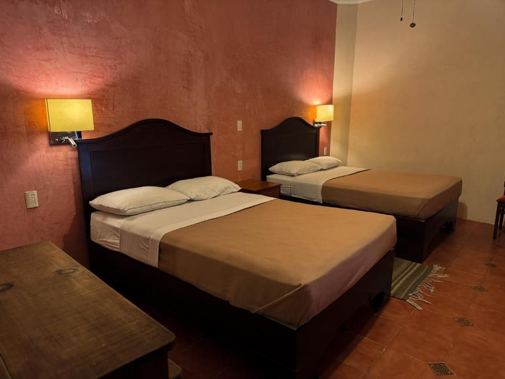 Habitación de hotel con dos camas individuales, una mesita y una lámpara de pared.