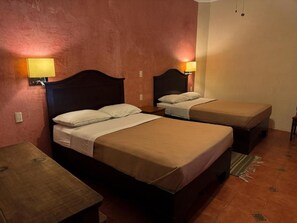A hotel room with two single beds, a small table, and a wall-mounted lamp.
