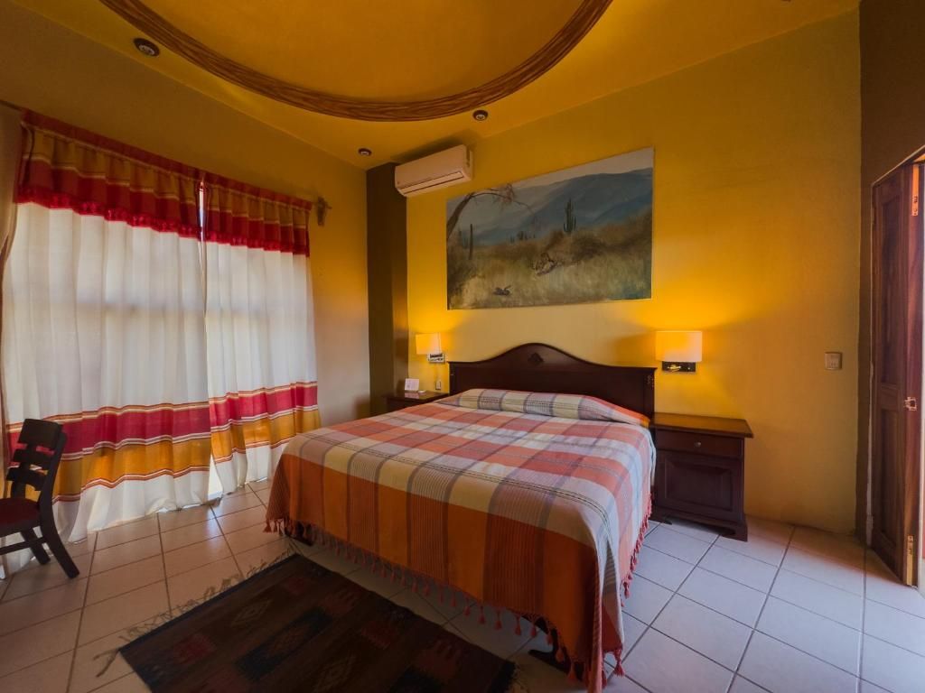 A hotel room with a bed, curtains, a painting, and a nightstand with a lamp.