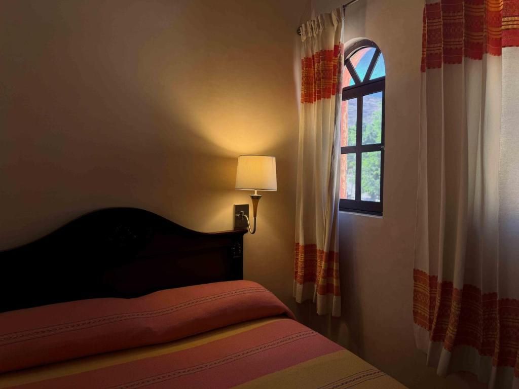 A room with a bed, a nightstand, a lamp, and a window with curtains.