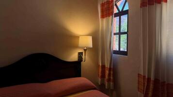 A room with a bed, a nightstand, a lamp, and a window with curtains.