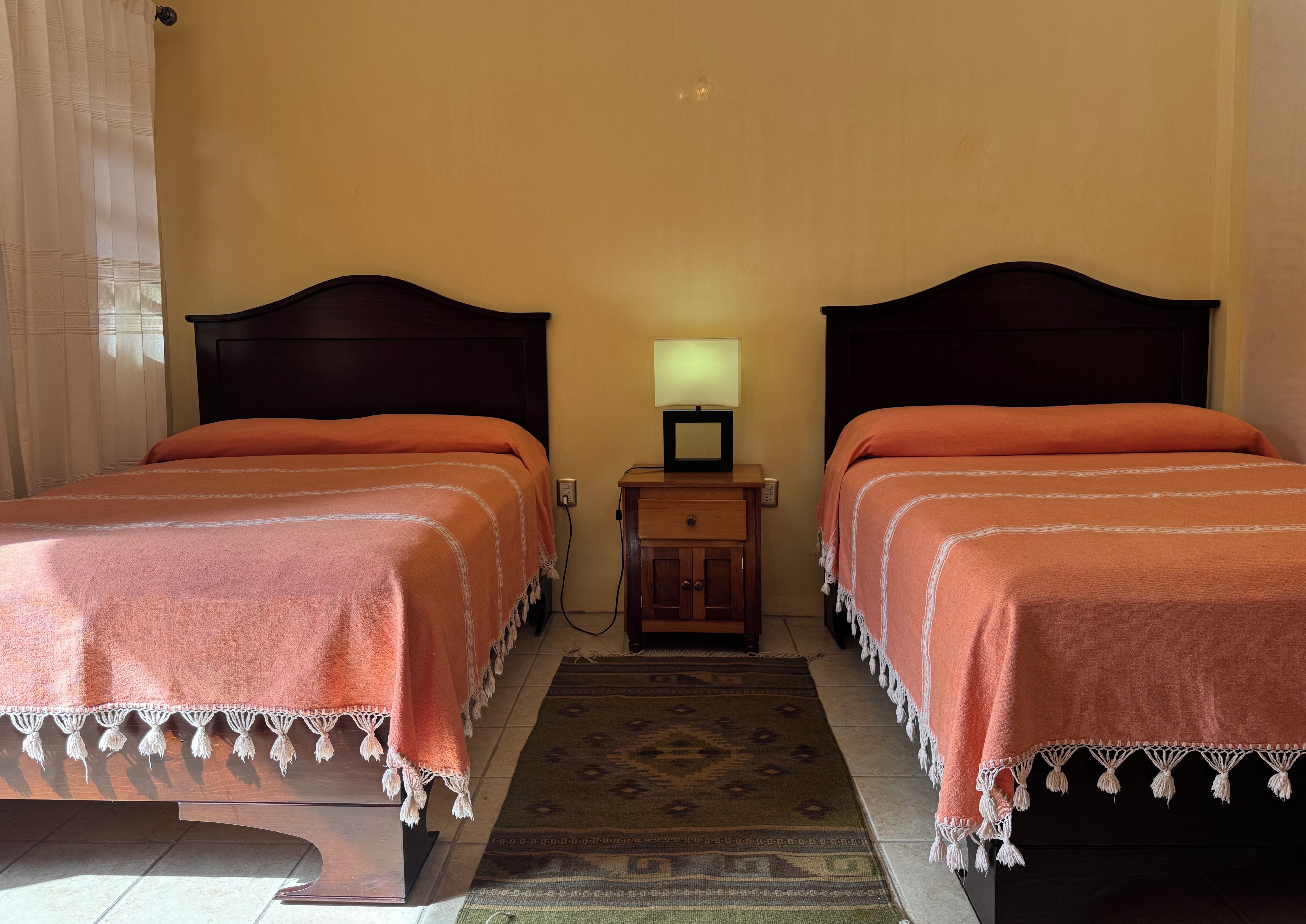 A room with two beds, a nightstand with a lamp, and a patterned rug.