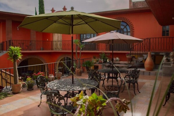 An outdoor patio with round tables and chairs, surrounded by potted plants and umbrellas.