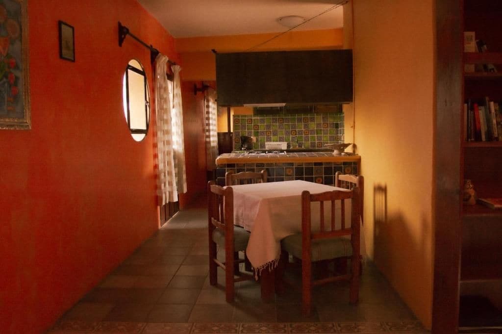 A narrow hallway with a dining table and chairs, a kitchen area with a tiled backsplash, and a bookshelf.
