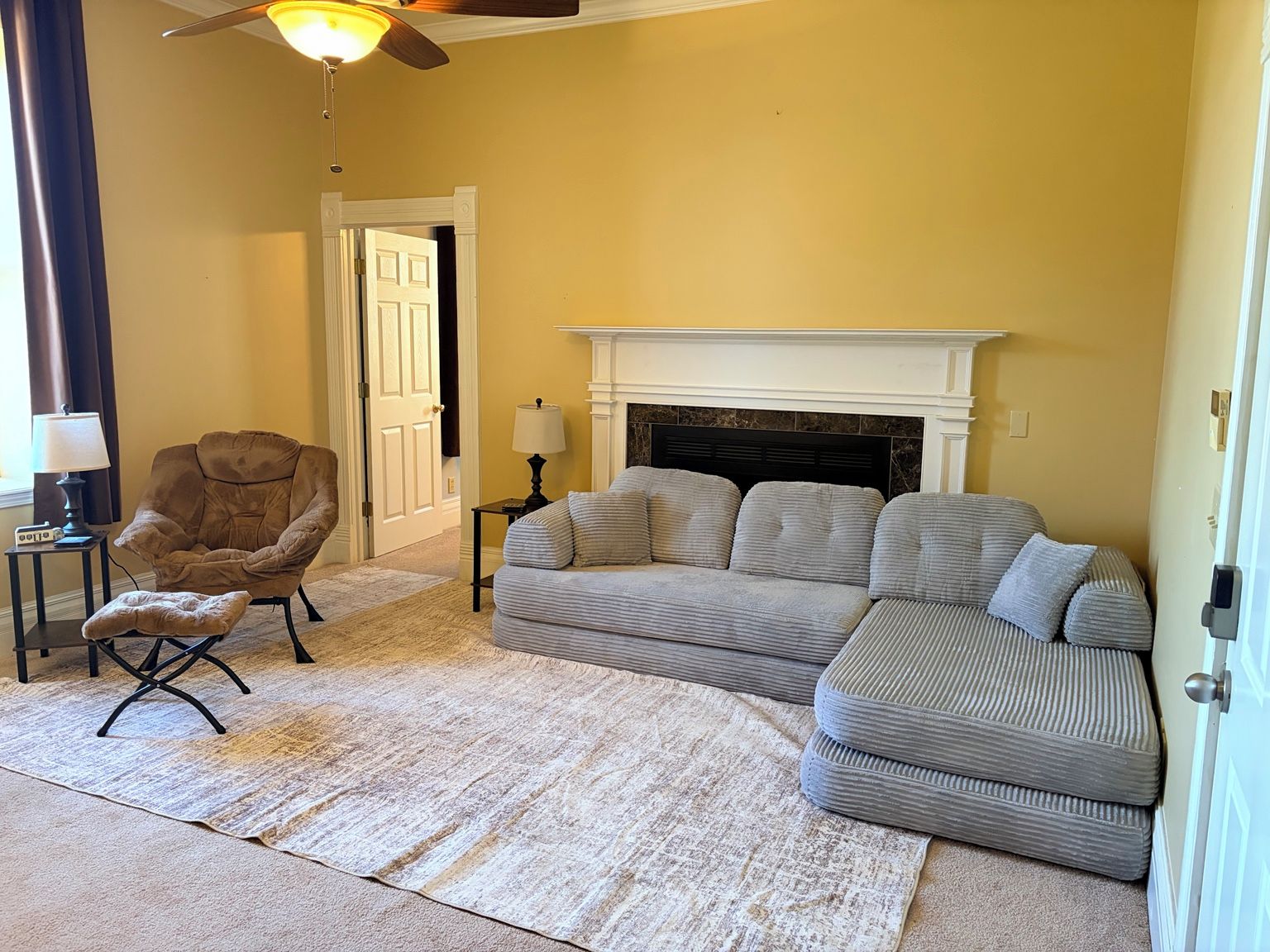 A living room with a sofa, armchair, and ottoman, a fireplace, and a ceiling fan.