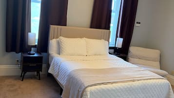 A bedroom with a bed, nightstands, a lamp, a chandelier, and curtains.