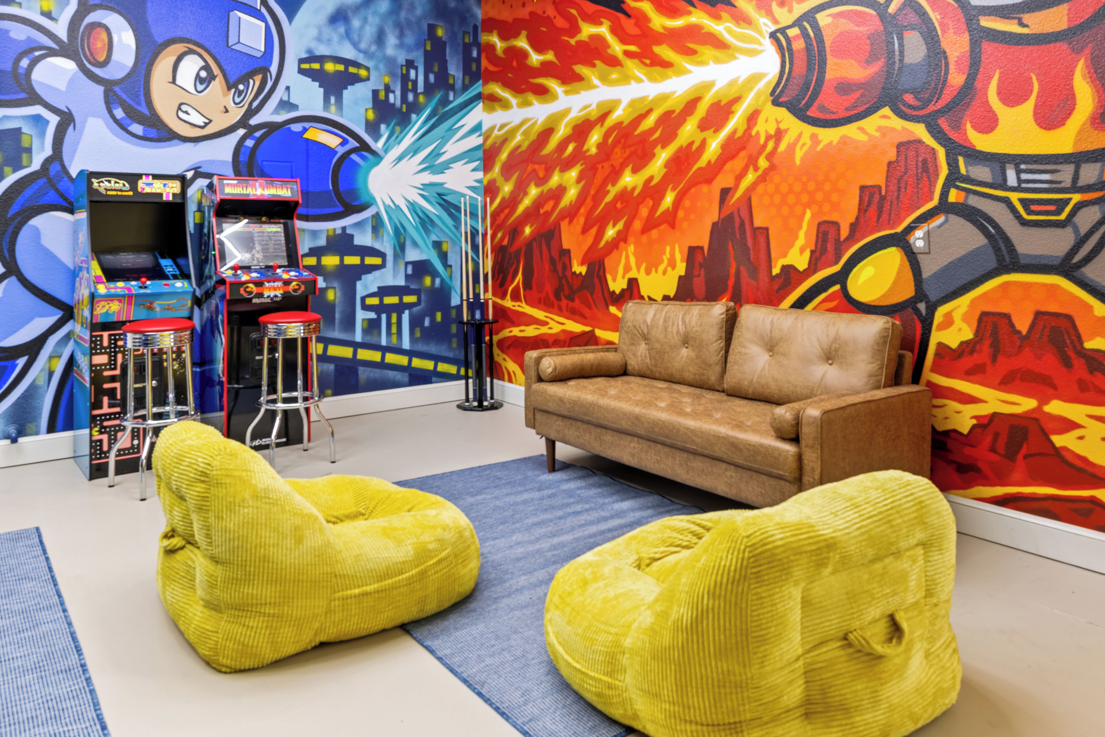 A room with a sofa, two bean bags, a pool table, and arcade machines.