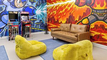 A room with a sofa, two bean bags, a pool table, and arcade machines.