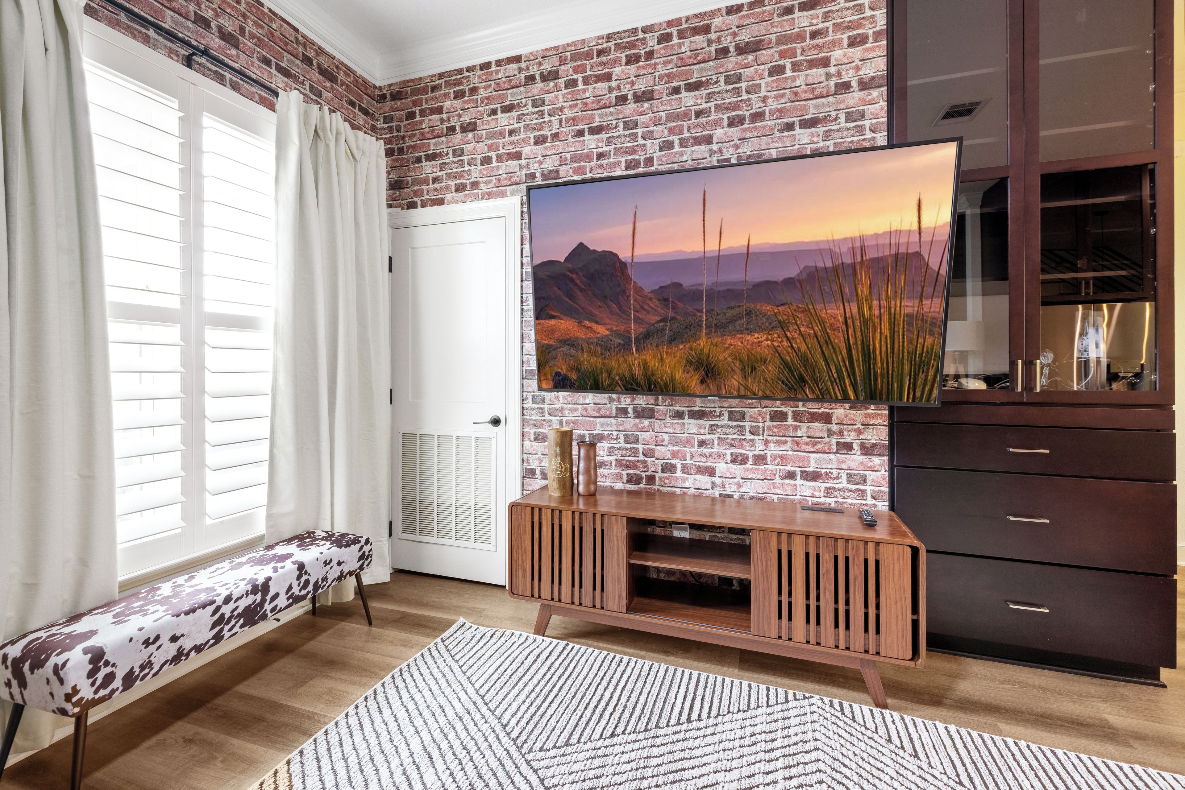Un salon avec un mur en briques, un téléviseur à écran plat, un meuble de rangement en bois et un banc.