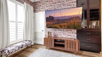 Un salon avec un mur en briques, un téléviseur à écran plat, un meuble de rangement en bois et un banc.