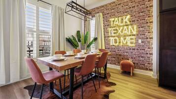 Un comedor con pared de ladrillo, un letrero de neón y una mesa con sillas.