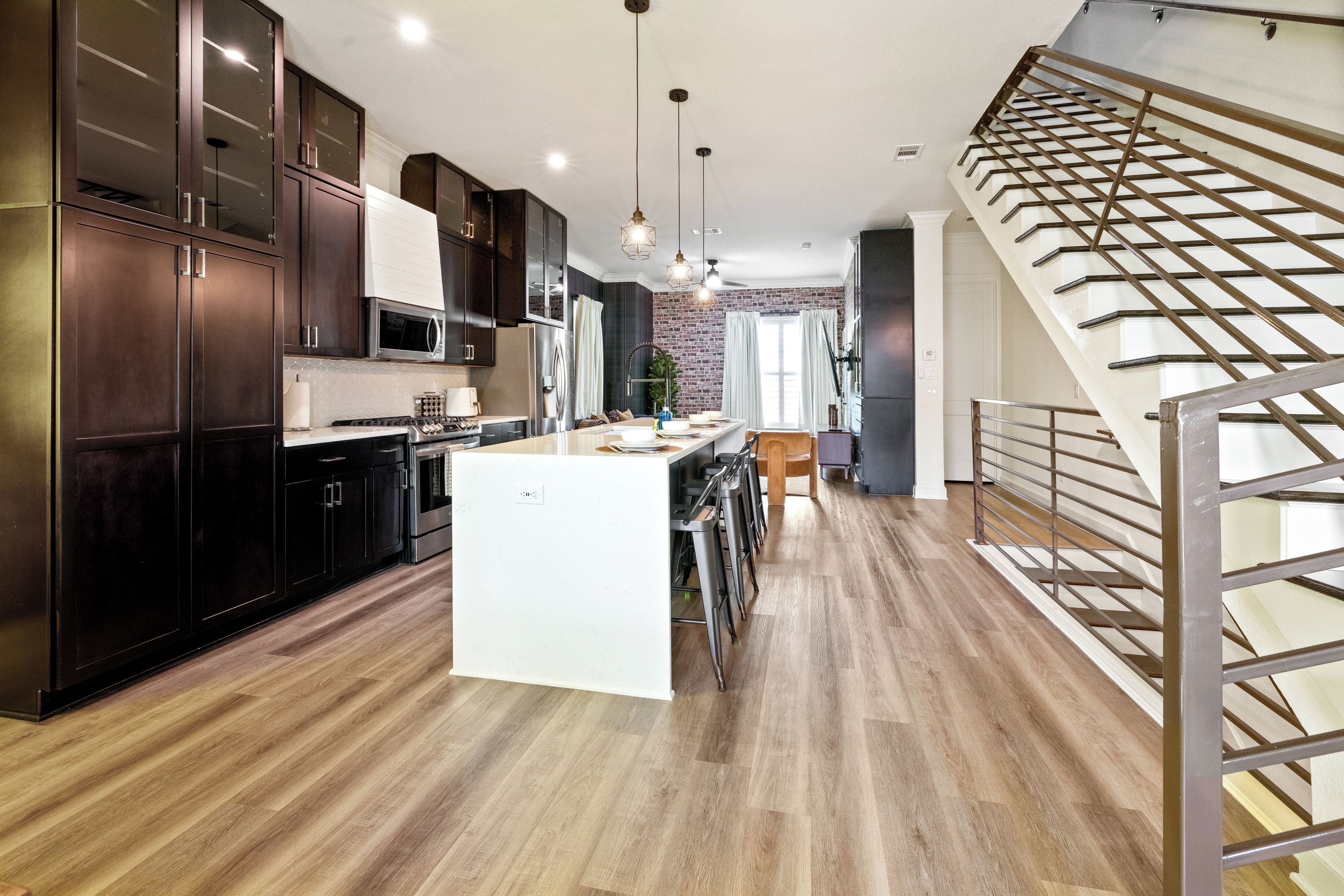 Una cocina moderna con armarios de madera oscura, una isla central, electrodomésticos de acero inoxidable y una escalera con barandilla metálica.