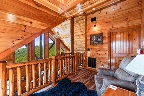 L'intérieur d'un chalet en bois, avec un balcon, un canapé et une cheminée.