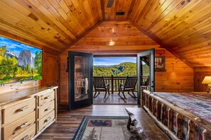 A cabin with a wooden interior, a balcony with chairs, and a large window with a mountain view. - Cubs Dream - Mountain Views・Private Indoor Pool・Theater・Hot Tub・Arcade & More! (Sevierville)