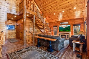 L’intérieur d’une cabane en rondins, avec une cheminée, un canapé, un téléviseur et un escalier.