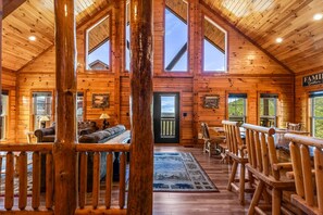 A log cabin interior with a high ceiling, wooden walls, a fireplace, a sofa, and a dining area. - Cubs Dream - Mountain Views・Private Indoor Pool・Theater・Hot Tub・Arcade & More! (Sevierville)