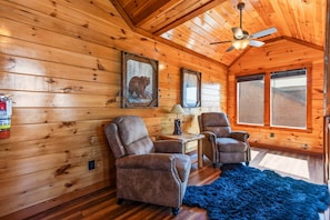 A log cabin interior with two leather chairs, a ceiling fan, a framed picture, and a window. - Cubs Dream - Mountain Views・Private Indoor Pool・Theater・Hot Tub・Arcade & More! (Sevierville)