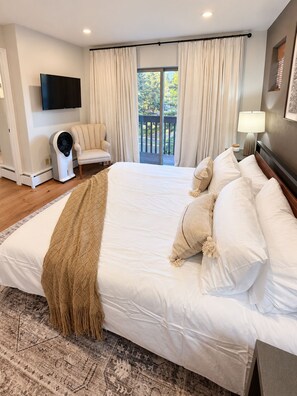 A hotel room with a large bed, a flat-screen TV, a ceiling fan, a chair, and a view of the outdoors through a sliding door. - Cozy + Spacious 3BR/3.5BA townhome in Edwards perfect for your mountain getaway (Edwards)