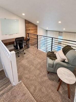 A modern living room with a sofa, a small table, a desk with a chair, a whiteboard, and a staircase leading to an upper level. - Cozy + Spacious 3BR/3.5BA townhome in Edwards perfect for your mountain getaway (Edwards)
