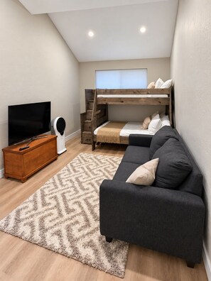 Een kleine kamer met een stapelbed, een slaapbank, een televisie en een houten dressoir.
