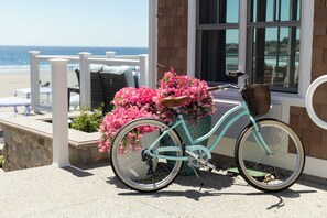 A turquoise bicycle with a basket and pink flowers, parked on a stone patio with a view of the ocean. - Inn at Good Harbor Beach (Gloucester)