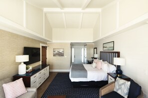 Una habitación de hotel con cama, mesitas de noche, televisor, escritorio y una silla.