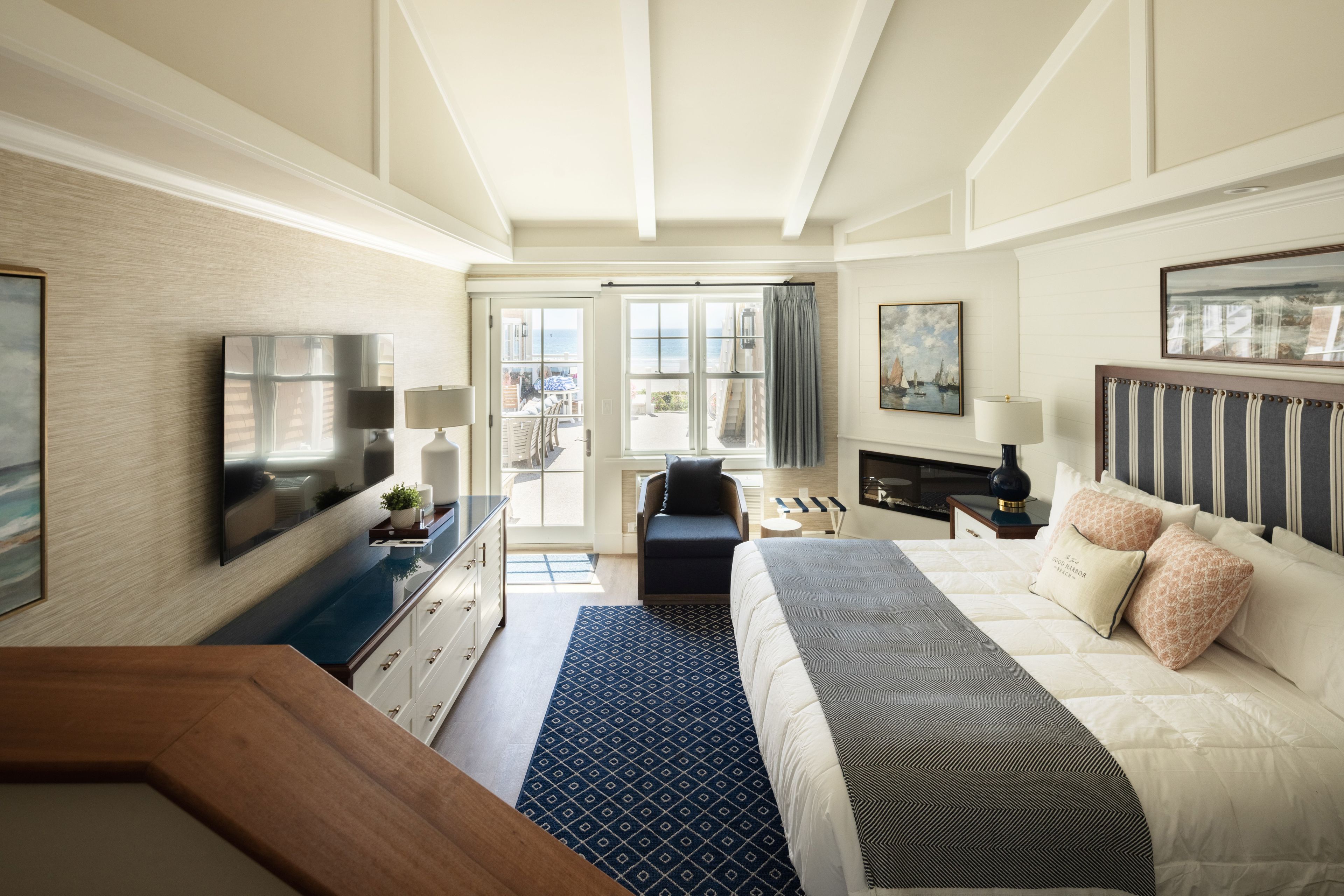 A hotel room with a bed, a desk, a TV, and a view of the sea.