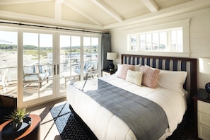 Habitación de hotel con una cama grande, vista a la playa y puerta corrediza de vidrio al exterior.
