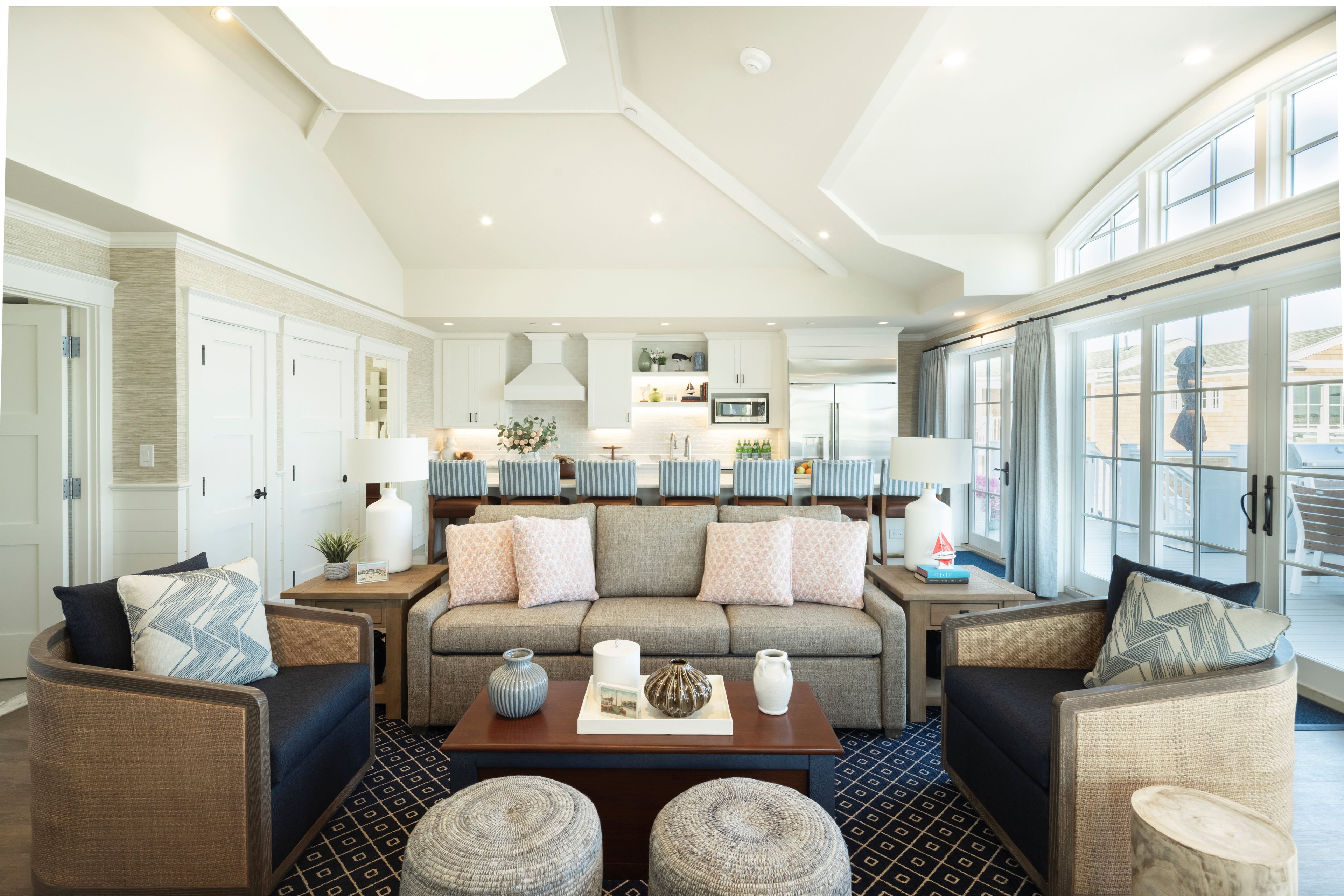 A well-lit living room with a high ceiling, a sofa set, a coffee table, and a view through large windows.