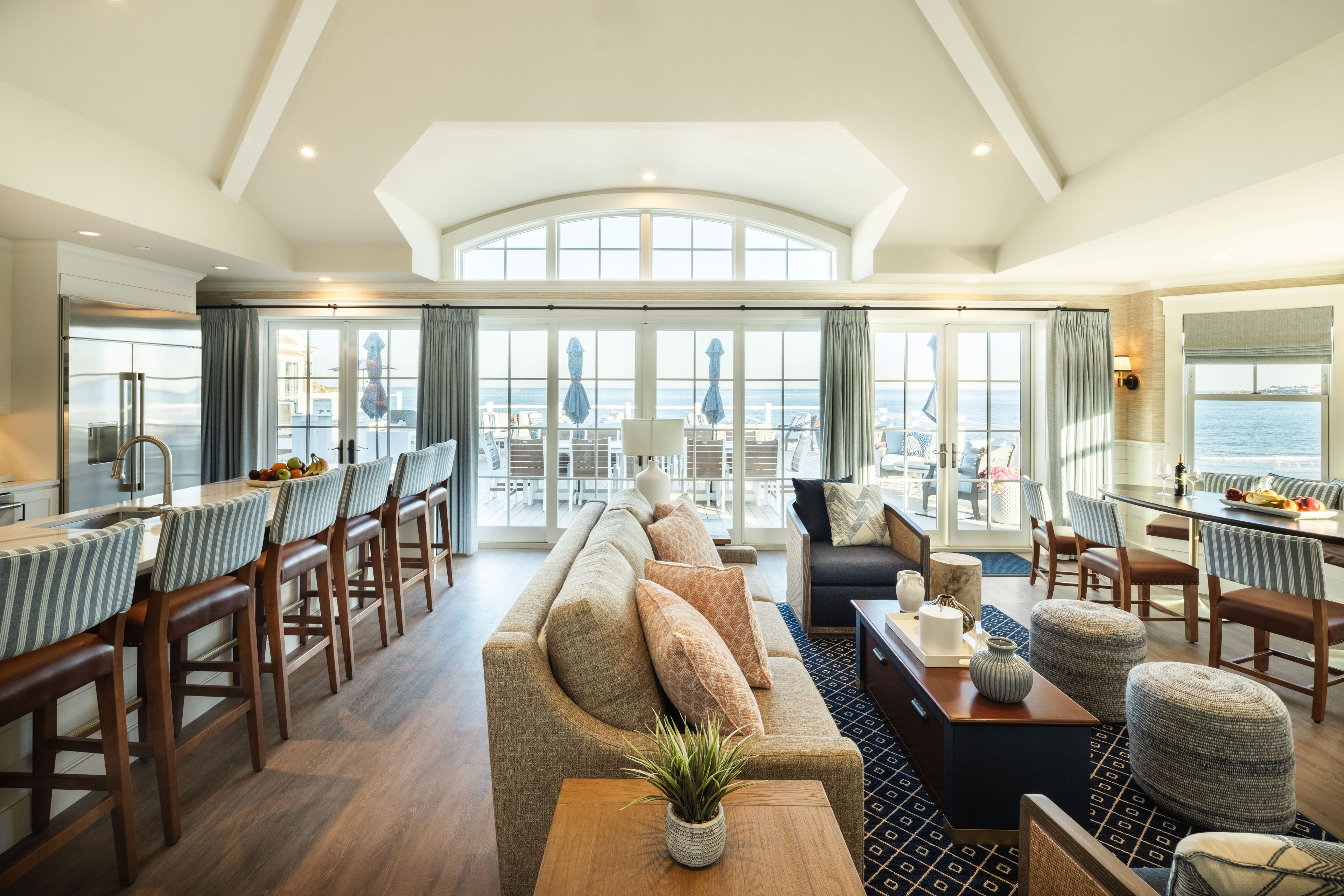 A spacious living area with a large window overlooking the sea, a dining area with bar stools, and a seating area with a sofa and armchairs.