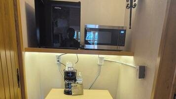 Une petite cuisine équipée d’un four à micro-ondes, d’une machine à café et d’un luminaire fixé au mur.
