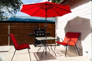 An outdoor patio with a red umbrella, two red chairs, and a barbecue grill. - Destination Red Raiderland - Walk to TTU - 2BR/2BA (Lubbock)