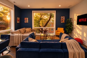 A modern living room with a large window, a sofa set, a coffee table, and a TV mounted on the wall.