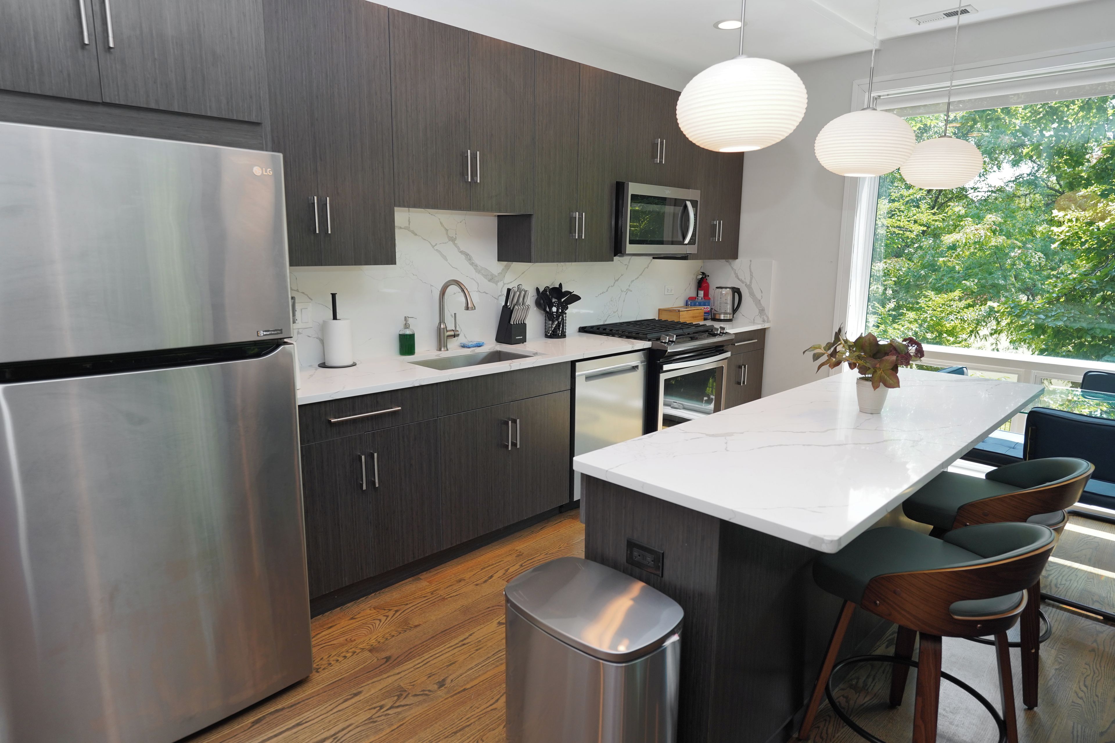A modern kitchen with dark cabinetry, stainless steel appliances, a marble backsplash, and a large island with bar stools.