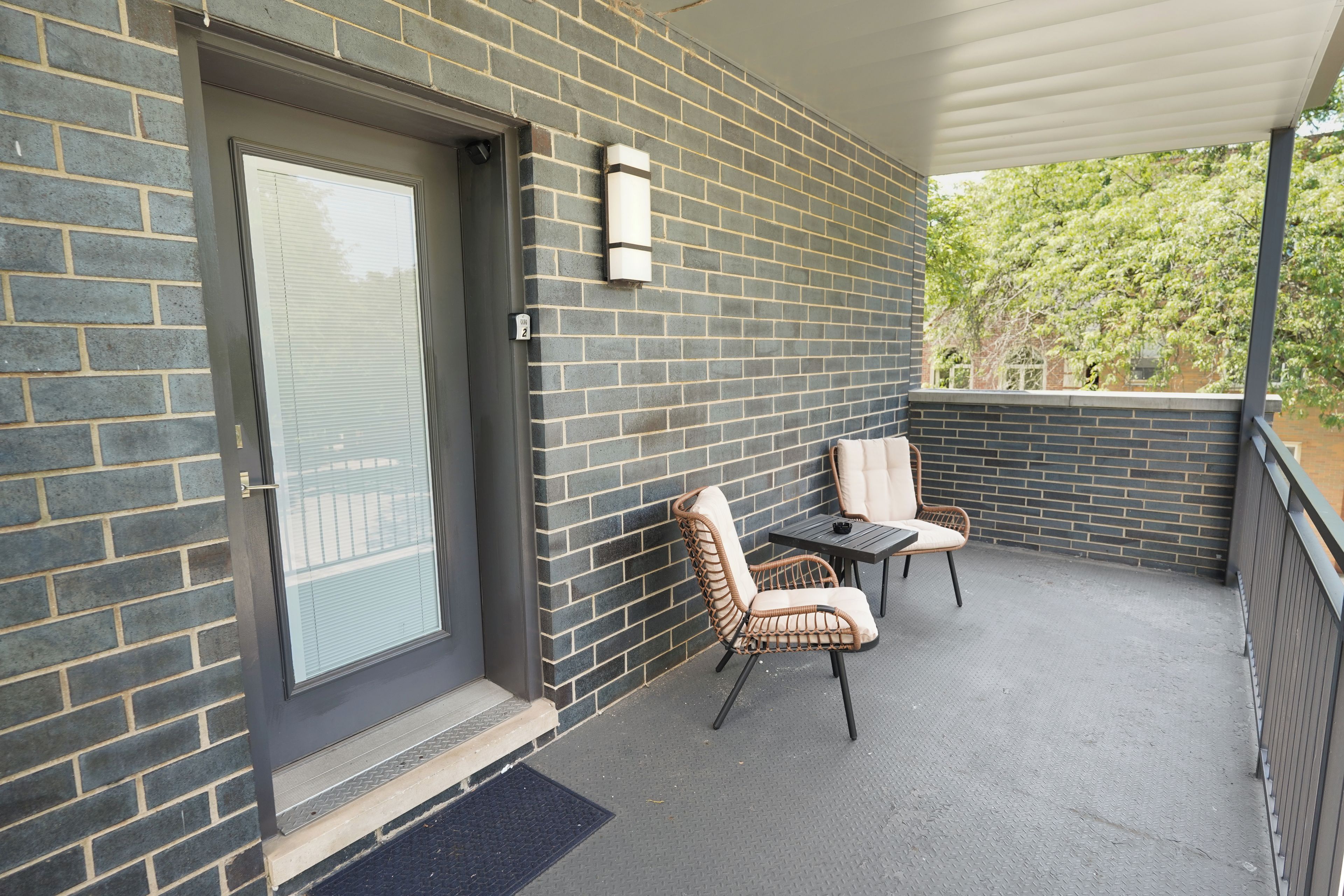 A balcony with a door, two wicker chairs, a small table, and a metal railing.