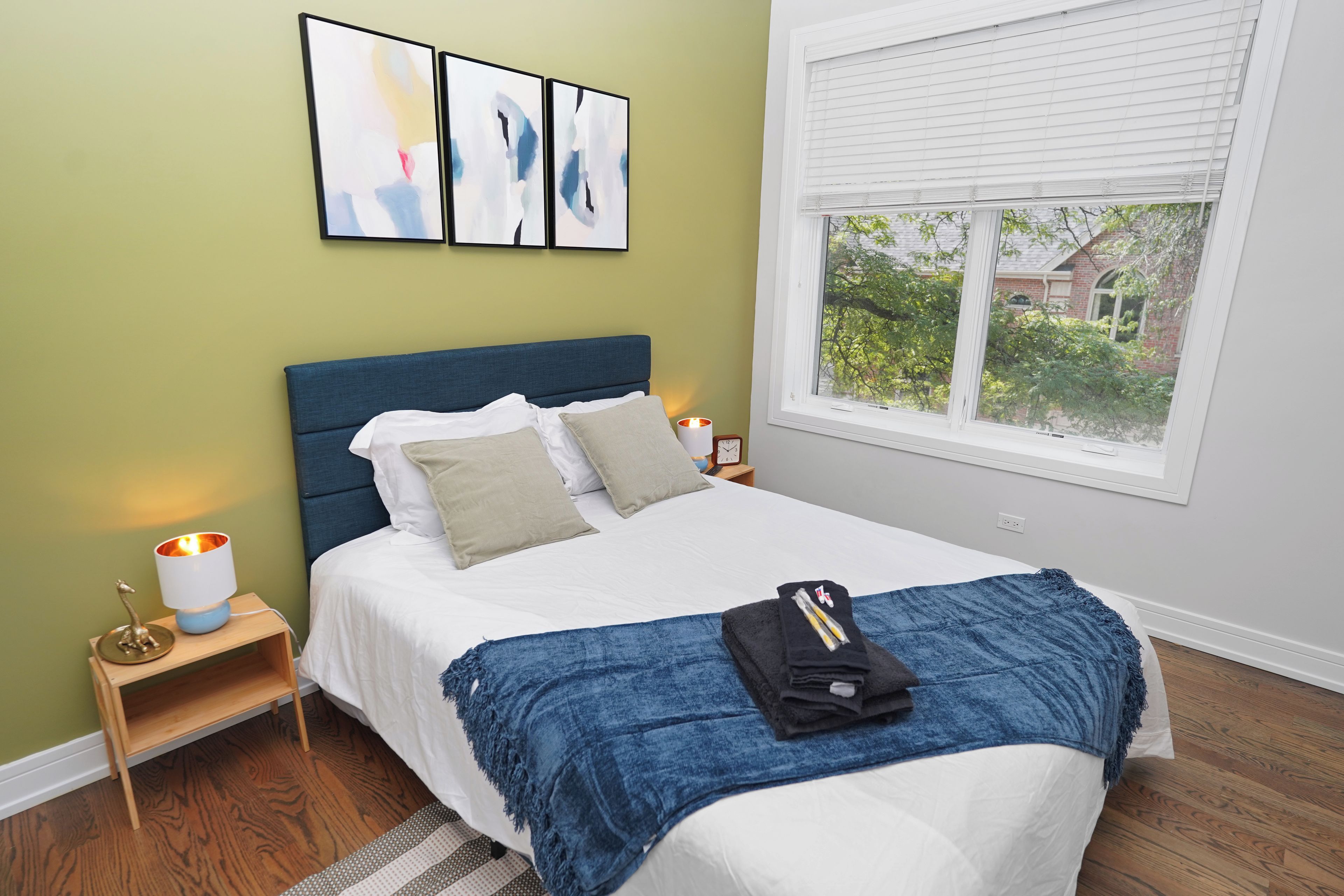 A neatly made bed with a blue blanket, a bedside lamp, and a clock on the nightstand.