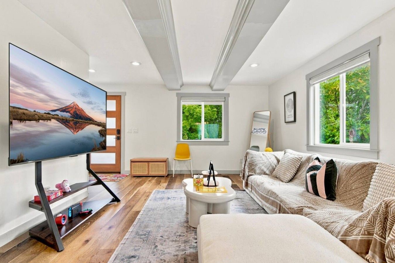 Una sala de estar moderna con un televisor de pantalla plana, un sofá, una mesa de centro y un ventanal con vistas a zonas verdes.