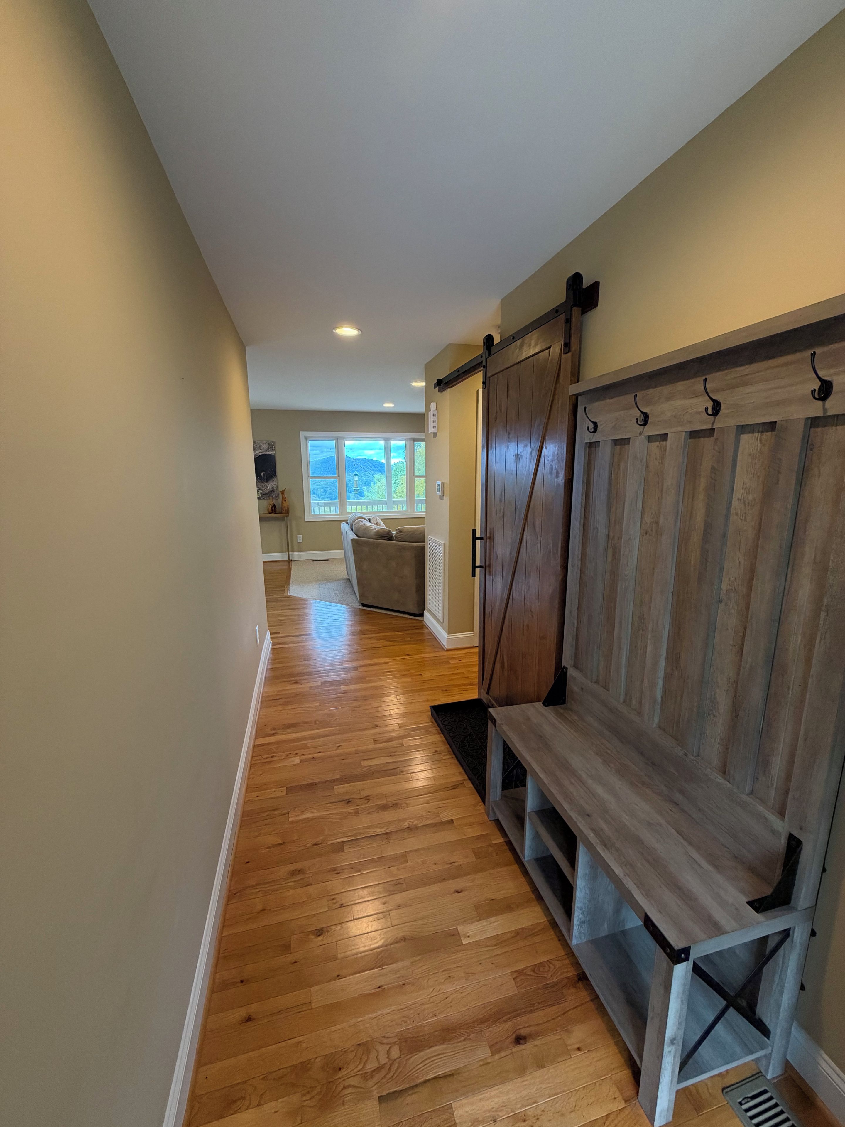 A hallway with wooden flooring, a bench, and a sliding barn-style door.