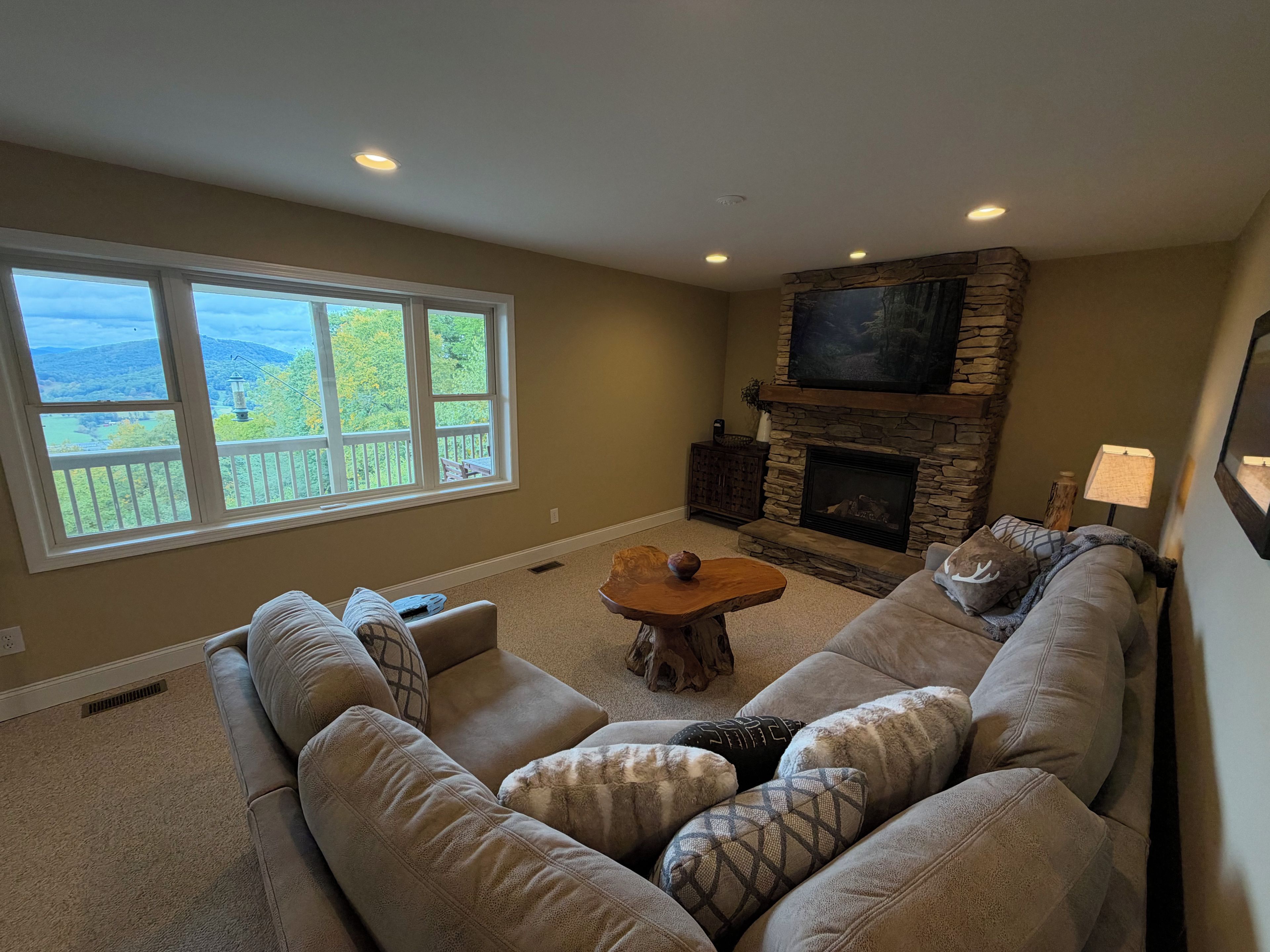 A living room with a stone fireplace, a large window with a view, and a cozy seating area.