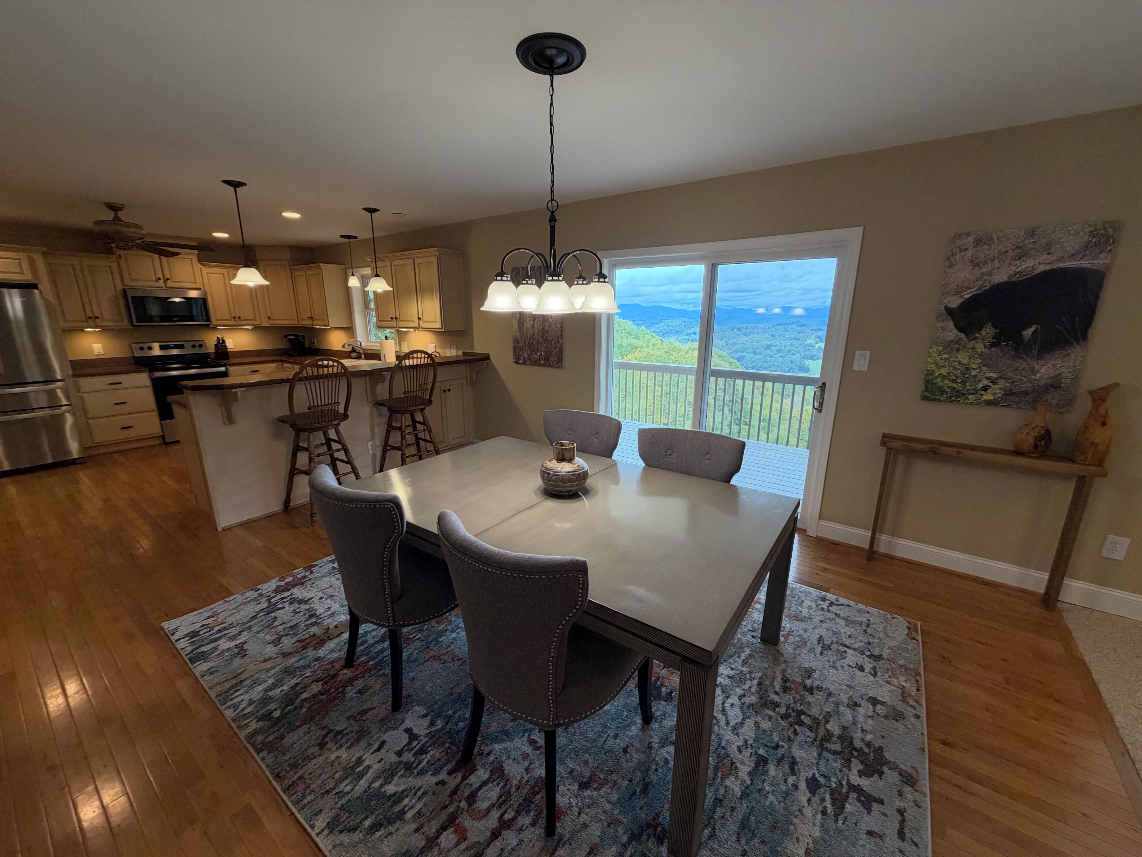 A modern kitchen with a dining area, large windows, and a view of the outdoors.