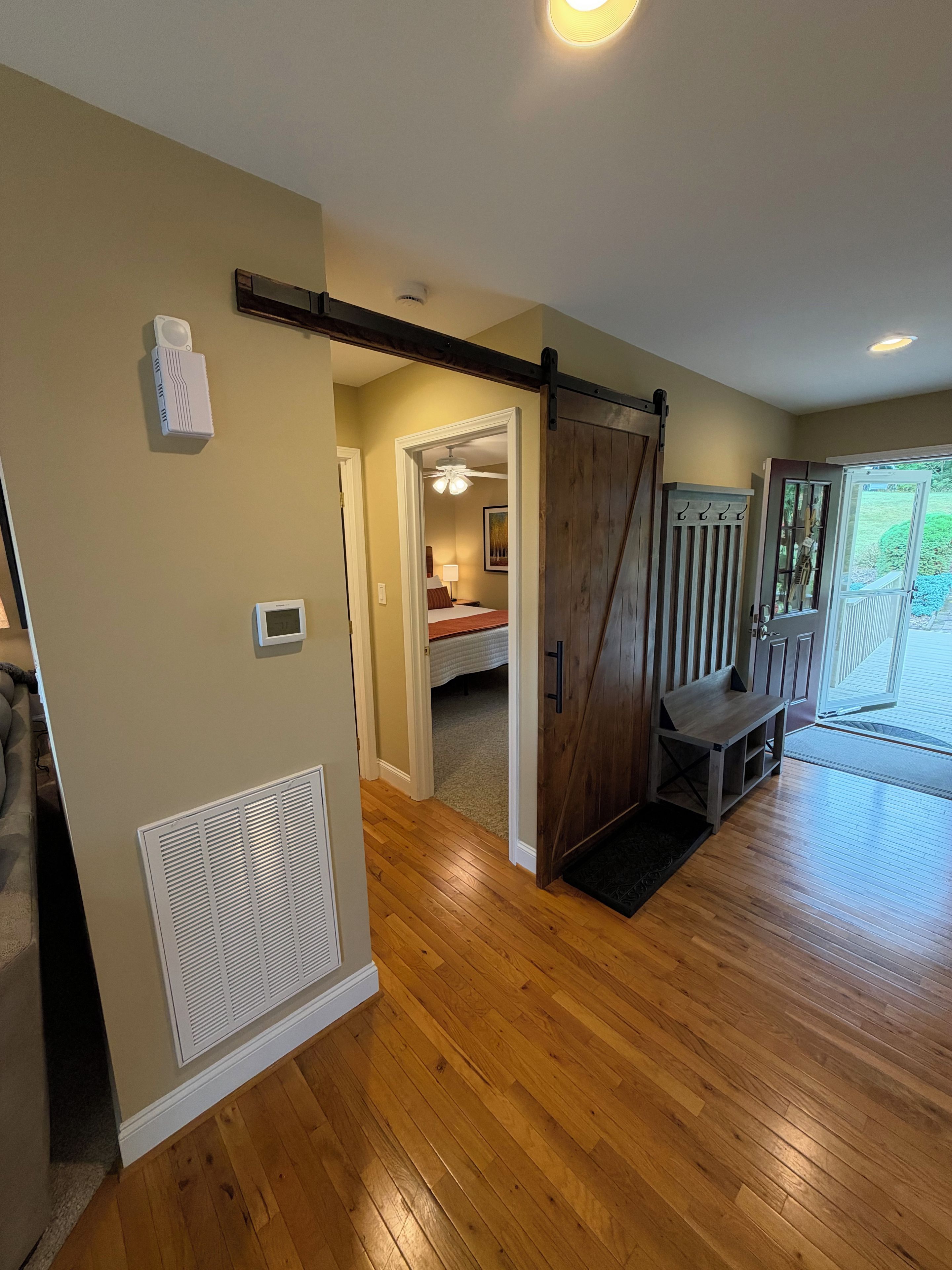 A room with wooden flooring, a sliding barn door, a ceiling fan, and a bed with a nightstand.