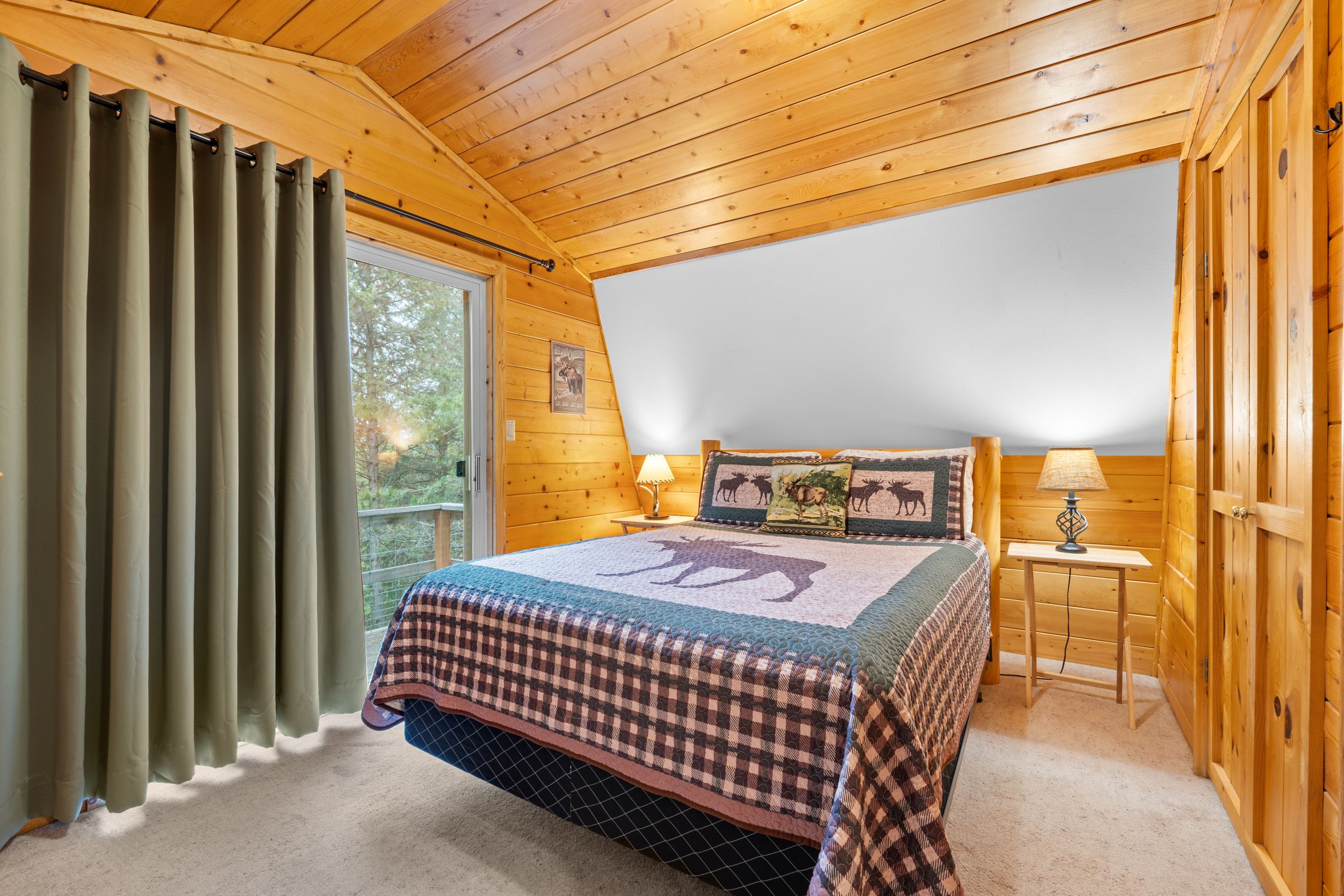 A bedroom with a bed, a window with curtains, a nightstand with a lamp, and a wooden ceiling.