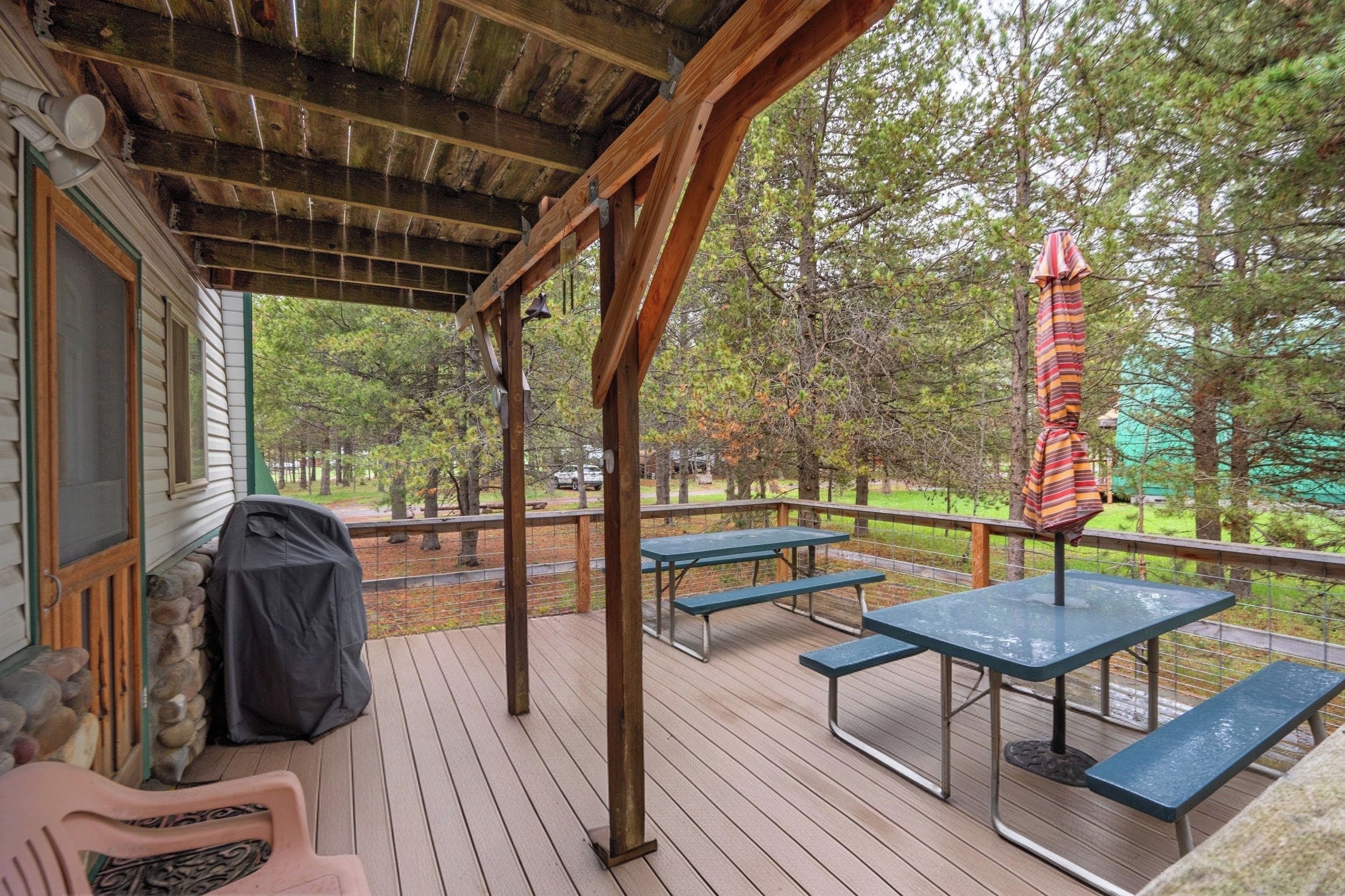 A covered outdoor deck with picnic tables and benches, overlooking a wooded area.