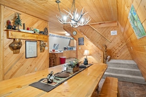 A cozy cabin interior with a wooden dining table, a chandelier, a kitchen area, and a staircase. - Beautiful 5-bedroom cabin perfect for your Island Park or Yellowstone getaway (Island Park)