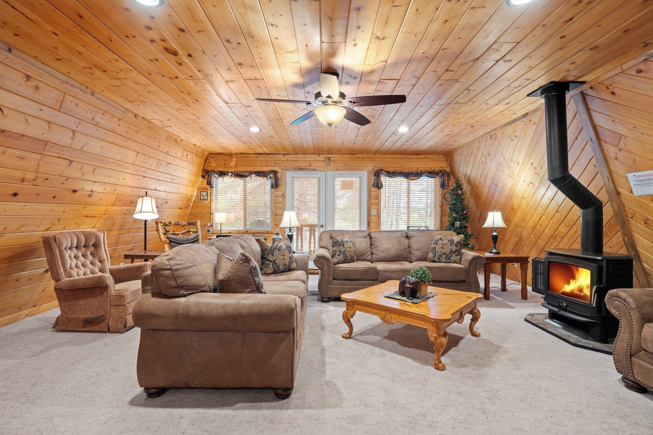 A cozy log cabin interior with a fireplace, leather furniture, and a ceiling fan.