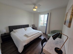 Habitación de hotel con cama, escritorio con silla, ventilador de techo y ventana con cortinas.