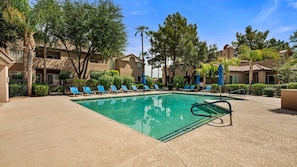 A swimming pool with lounge chairs and umbrellas, surrounded by buildings and trees. - Roadrunner Haven — warm and welcoming Monthly Rent (Scottsdale)